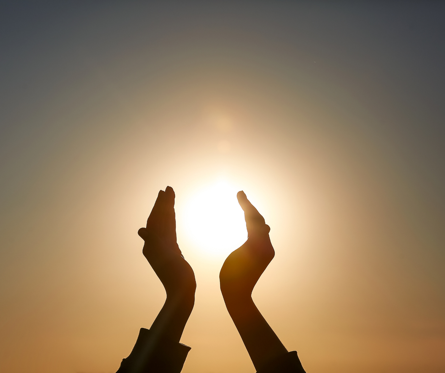 Open hands reaching towards the sun at sunset
